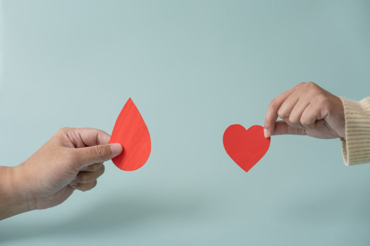 Blood donation or medical surgery concept. Human holding small piece of paper blood sign and a red heart shape.