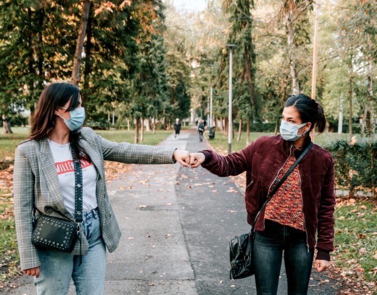 friends-in-city-fist-bump-greeting-in-the-park-cor-L7HPQ52